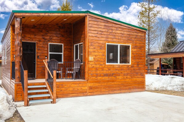 Chalet with a front balcony and parking space for two vehicles.