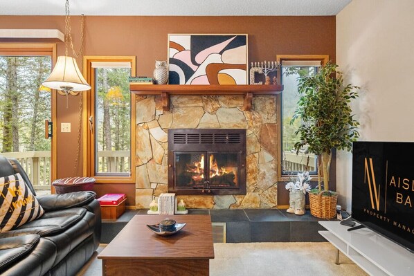 Living room with a 55" smart TV with cable, wood-burning fireplace, cozy seating options & walkout access to the balcony.
