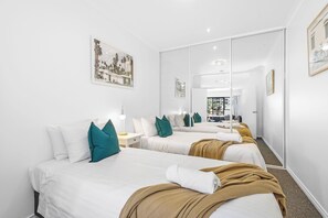 Enjoy a spacious bedroom with two twin beds, each with teal pillows and a golden throw, plus mirrored closets that amplify the space.