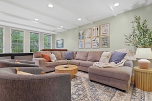Primary living room with large sectional seating, bar top table with barstools, 60" smart TV, shuffleboard table, and kids toys
