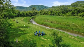 The grassy area down by the water includes an 8 person fire pit, yard games, wicker swing, kayaks, and tubes.