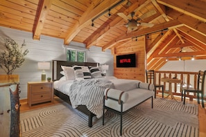 BIG CABIN - Loft bedroom with king size bed, 50" smart TV, bistro table for coffee or a board game, dresser, portable fan, overhead fan, and an ottoman.