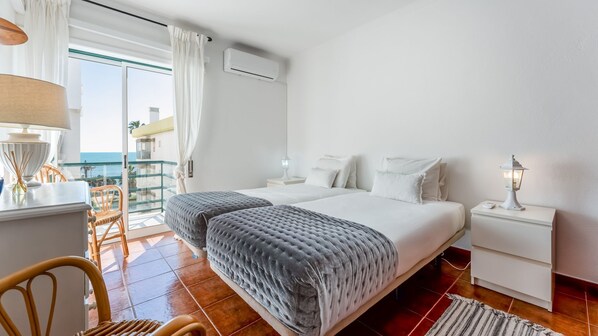 Relax in a serene coastal bedroom with twin beds, air conditioning, and balcony access overlooking the ocean. #OceanRetreat #CoastalCalm #SeaBreezeSleep