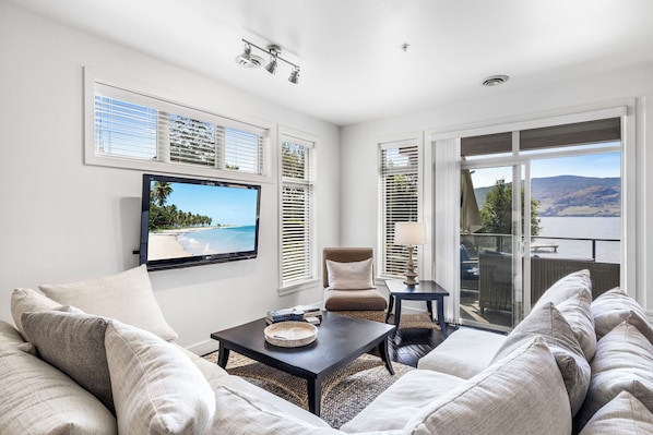 Modern living room with a sectional sofa, coffee table, and mounted TV, opening up to a view of the outdoors through the sliding glass door.