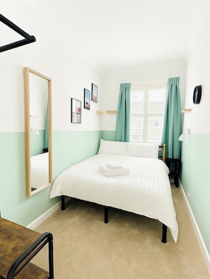 Cozy and bright double bedroom with fresh green accents, plush carpet, and a large window flooding the room with natural light. (1)