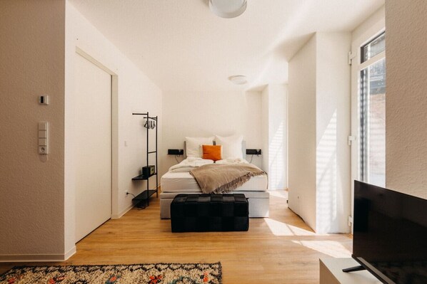Gemütliches Schlafzimmer mit warmen Akzenten. Große Fenster fluten den Raum mit Licht, während das bequeme Bett und weiche Textilien für erholsame Nächte sorgen. Perfekt für entspannte Stunden – mit direktem Zugang zum Wohnbereich & TV-Genuss!