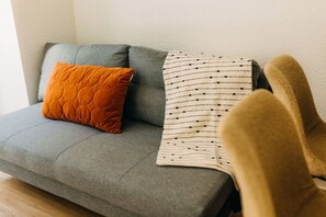 Die stilvolle graue Couch mit ihren weichen Kissen und der dezenten Decke lädt zum Entspannen ein. Das warme Orange des Kissens sorgt für einen charmanten Farbakzent und schafft eine gemütliche Atmosphäre im Wohnbereich.