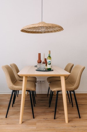 Ein stilvoller Essbereich mit natürlicher Eleganz. Der Holztisch, die bequemen Bouclé-Stühle und die geflochtene Pendelleuchte schaffen eine warme Atmosphäre – perfekt für gemütliche Abende bei einem Glas Wein.