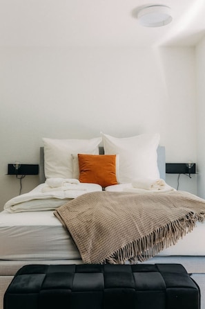 Ein Bett zum Träumen: Hochwertige Bettwäsche, sanfte Farben und weiche Textilien sorgen für pure Entspannung. Das elegante Design wird durch dezente Lichtakzente und die stilvolle Ottomane am Fußende abgerundet.