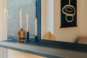 Minimalistische Eleganz: Schlichte Kerzenhalter und eine Glasvase setzen stilvolle Akzente auf der dunklen Arbeitsplatte. Das warme Sonnenlicht betont das harmonische Zusammenspiel von Farben und Materialien und schafft eine gemütliche Atmosphäre.