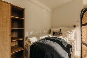 Das Sonnenlicht tanzt auf dem kuscheligen Bett und schafft eine warme, einladende Atmosphäre. Hochwertige Bettwäsche, natürliche Materialien und ein stilvoller Kleiderschrank sorgen für Komfort und Ordnung – perfekt für eine erholsame Nacht.