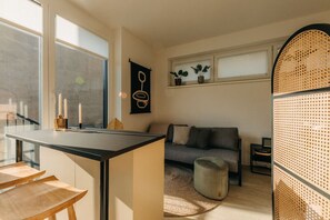 Sonnenlicht flutet den Raum und hebt das stilvolle Design hervor. Die gemütliche Sitzecke mit modernem Sofa und Naturmaterialien schafft einen perfekten Ort zum Entspannen oder Arbeiten – stilvoll, ruhig und inspirierend.