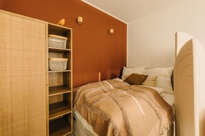 Einladende Ruheoase: Der rustikale Schrank, die warmen Erdtöne und die gemütliche Bettwäsche schaffen ein Gefühl von Geborgenheit. Kleine Details wie der gelbe Vogel und die weichen Kissen setzen fröhliche Akzente in diesem harmonischen Raum.