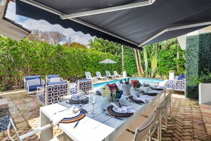 Al fresco perfection! 🌺 Dine poolside surrounded by lush greenery, vibrant blooms, and chic coastal vibes. With a heated pool, loungers, and tropical privacy, your slice of paradise awaits.