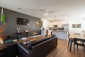 The photo depicts a spacious living room that combines comfort and elegance. A large sectional sofa upholstered in gray fabric faces a modern fireplace framed by a sleek mantel. Above the fireplace hangs an abstract painting that adds a splash of color to the neutral tones of the room. Floor-to-ceiling windows offer a panoramic view of the city skyline, allowing natural light t...