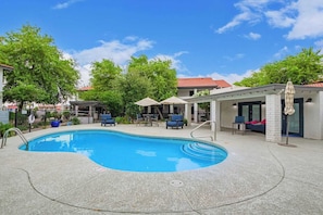 This inviting backyard boasts a sparkling swimming pool, perfect for spending hot summer days. The comfortable chairs and umbrellas provide a place to relax and unwind.