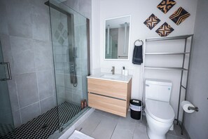 This modern bathroom features a glass shower with a patterned floor, a wooden vanity topped with a white basin, and an illuminated mirror. It blends aesthetics with functionality seamlessly