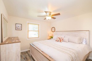 King bedroom with ceiling fan, dresser, and mirror. Reading lamp on nightstand. 