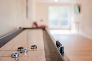 The first of two rec rooms features table shuffleboard and a smart tv with a couch.