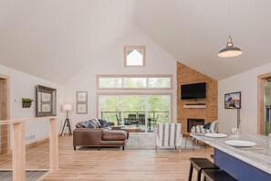 Open concept living room, kitchen, and dining room with modern decor. Features a gas fireplace below a smart tv. 