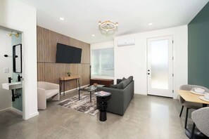 The living room features a comfortable couch, accent chair, stylish coffee table, and soft lighting from a floor lamp. A large Smart TV is perfect for relaxing with your favorite shows, making this space ideal for winding down or gathering together.