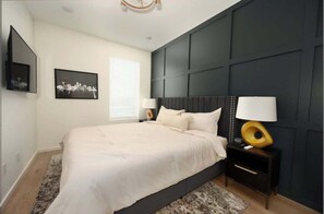 The main bedroom offers a restful retreat with a plush king-size bed, cozy linens, and a large Smart TV for relaxing nights in. Thoughtful touches like bedside lamps and white noise machine ensure a peaceful sleep.