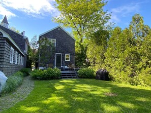 The rear of the cottage has a deck with dining area, gas grill, and a small lawn