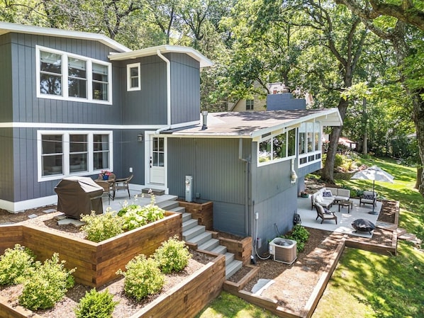 Back side of home with propane grill and upper deck with smaller table and chairs.