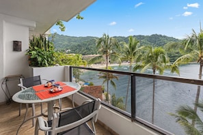 Outdoor balcony dining area with a view of lush greenery and ocean.