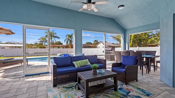 The screened-in back porch is furnished with a cushioned outdoor sofa, lounge chair, and dining table.