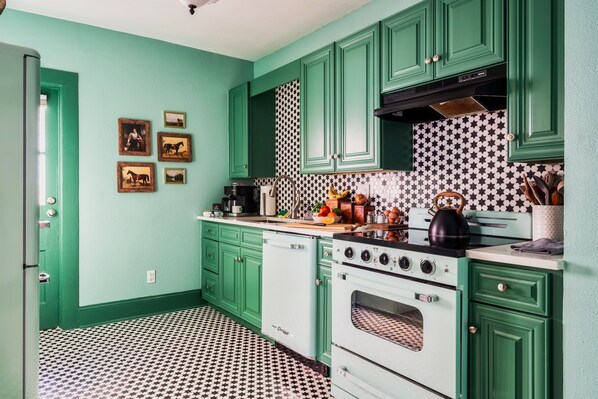 [Kitchen| Step into a retro-inspired kitchen with vibrant green cabinetry, a charming vintage-style oven, and striking black-and-white star-patterned tile flooring