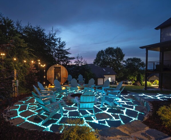 Picture yourself lounging in turquoise Adirondack chairs on a bioluminescent-inspired glowing stone patio, encircling a roaring fire pit. Unwind in the cozy barrel sauna as string lights twinkle like fireflies beneath a starry sky. 