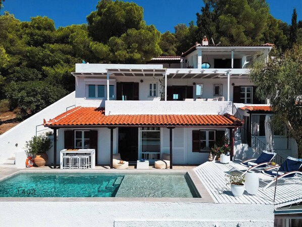The front view of the villa, where all the levels can be seen, as well as the terraces, the delightful swimming pool and the lush greens surrounding the villa