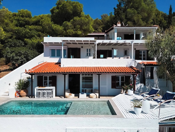 The front view of the villa, where all the levels can be seen, as well as the terraces, the delightful swimming pool and the lush greens surrounding the villa