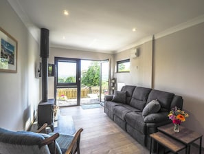 Lounge area with sofa, log burner, coffee table, doors to garden