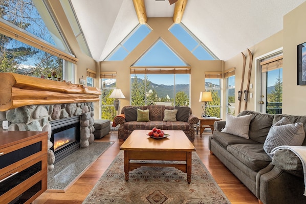 Bright, open-concept living area features high ceilings, log beams and large picture windows with scenic views