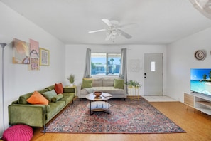 This living room combines modern style with cozy charm, featuring colorful accents, tasteful décor, and plenty of natural light to create a welcoming and vibrant atmosphere.