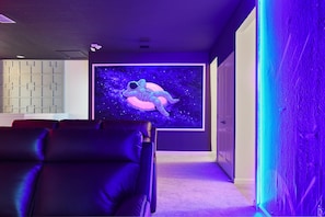 Futuristic theater room with neon lighting, cosmic art, and cozy seating.