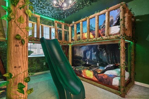 Dinosaur-themed bunk room with slide, leafy decor, and immersive wall murals.