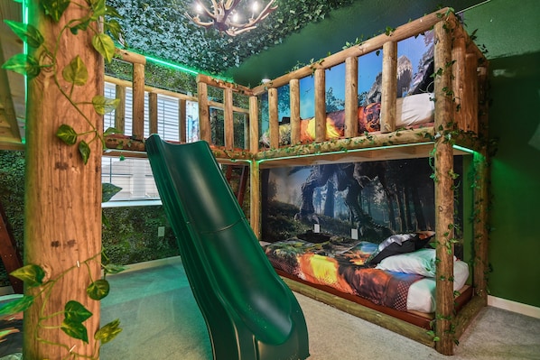 Dinosaur-themed bunk room with slide, leafy decor, and immersive wall murals.