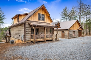 The cabin is on the left side. The game room/man cave is the building on the right. The driveway is gravel. Parking is flat.