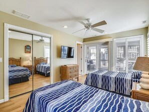 This coastal-themed bedroom features two twin beds with ocean-inspired bedding and direct access to a private patio through sliding glass doors.