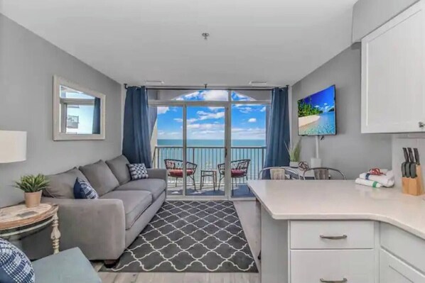 The spacious living room, flooded with natural light, features floor-to-ceiling windows and Slider Doors that frame a panoramic vista of the serene ocean horizon.