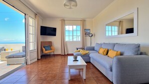 The living room at Desertas Vista Ninho offers a comfortable, stylish sofa, a Smart TV for your entertainment, and large windows that frame a beautiful view of the ocean. #oceanview #bigsofa #freewifi