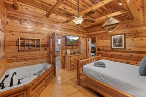 This upstairs master suite features exposed beams, a flat-screen TV, and a spacious open layout.