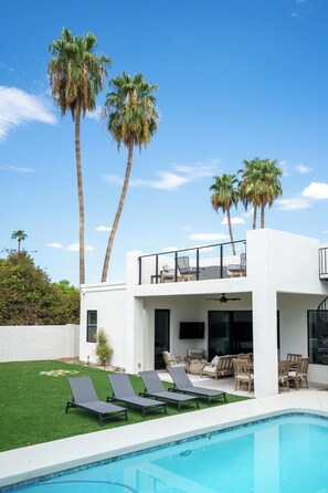 Backyard pool with loungers and rooftop patio surrounded by palms.