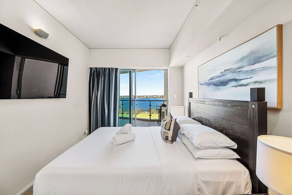 Breathtaking waterfront views to enjoy from your bed. The focus is on the well-made bed, promising a restful night's sleep, while the room's clean lines and contemporary art create a calming atmosphere.