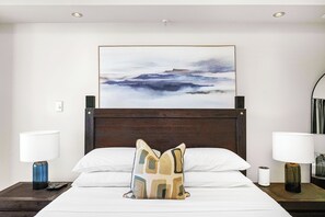 Seeking a peaceful and relaxing retreat.  A tranquil bedroom, designed for relaxation and comfort. The focus is on the inviting bed, adorned with soft white linens and a decorative geometric pillow, creating a peaceful haven for rest.