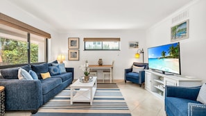 Bright and breezy coastal living room featuring a bold navy sofa, streaming TV, a collection of books, and a charming breakfast nook—perfect for relaxed mornings and cozy evenings.