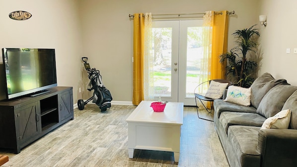 Open living room with double doors leading to covered and furnished patio.
